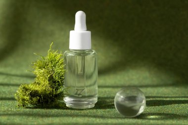 Doğal güzellik kozmetik serumu şişesi. Üzerinde yeşil doğal arka plan ve gölgeler var..