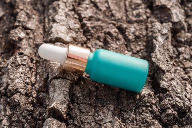 Kozmetik serumu şişesi, ağaç kabuğu arka planında pipeti olan maket.