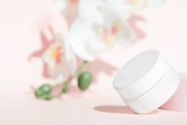 Çiçeksel pembe arka planda kozmetik krem kavanozu modeli.