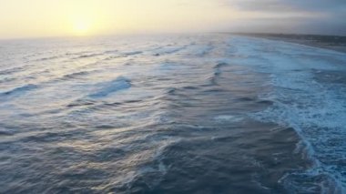 Okyanus dalgalarının üzerinde gün batımı, altın saat boyunca denizin üzerinde uçmak. Denizde köpüren ve sıçrayan dev dalgalar. Sinematik drone çekimi, günbatımı dalgalı deniz manzarası
