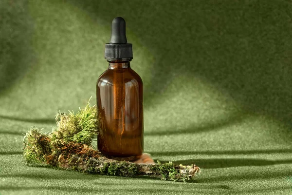Amber glass bottle with serum, essential oil, anti aging collagen cosmetic beauty product among the green mossy backdrop. — Stock Photo, Image