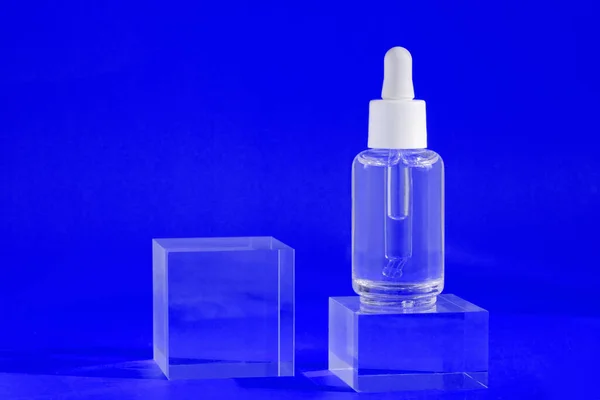 Suero antienvejecimiento con colágeno y péptidos sobre cubos acrílicos azules con sombras. Maqueta de aceite de ácido hialurónico. — Foto de Stock