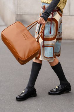 Paris, Fransa - 11 Mart 2025: Kahverengi dikdörtgen Miu Miu çanta kabartmalı logo, siyah mokasen ayakkabı ve retro etek. Sokak tarzı kıyafet ayrıntıları.