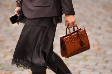 Paris, Fransa - 6 Ekim 2025: Kadınlar Saint Laurent kahverengi deri çanta giyerler. Moda kıyafet çantası detayı, sokak tarzı aksesuar.