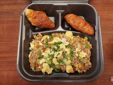 Tahta bir masada üzerinde kruvasan olan siyah bir konteynırda kızarmış pirinç.