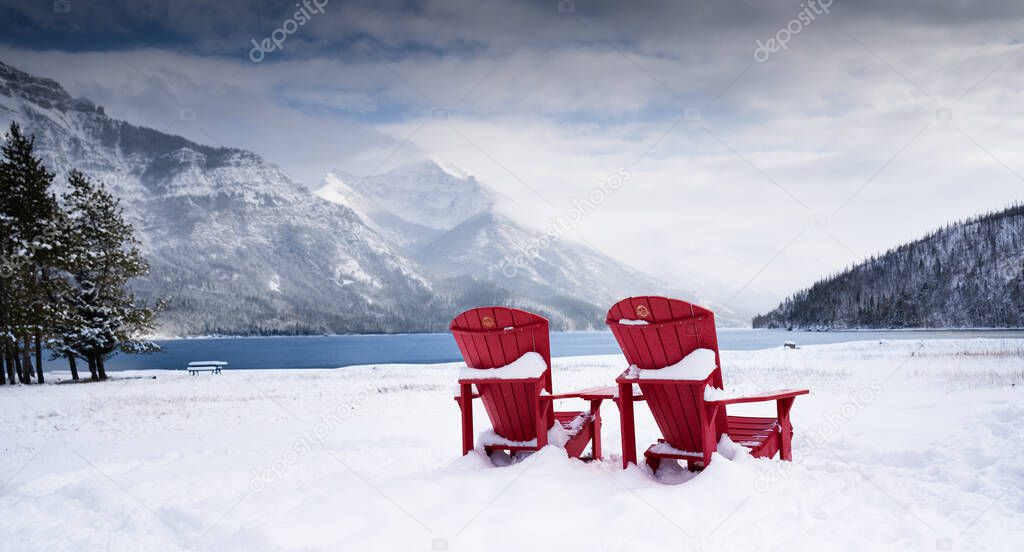 A pair of wooden chairs overlooking Waterton Lakes National Park Canada during the winter with a glacier lake