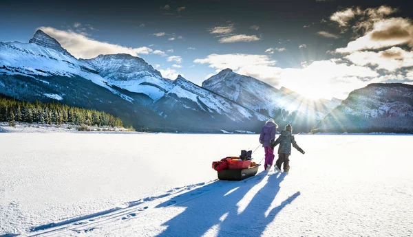 加拿大落基山脉Peter Lougheed省立公园内 两个孩子在结冰的冰天雪地上拖着一辆装有冰块渔具的雪橇 — 图库照片