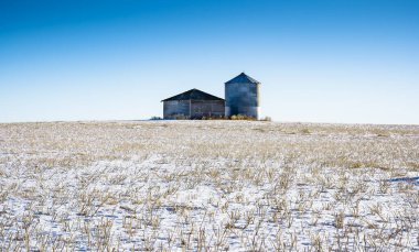 Boş bir tahıl ambarı ve depolama hangarı Rocky View County Alberta 'daki Kanada ovalarında hasat edilmiş kar tarlasında duruyor..
