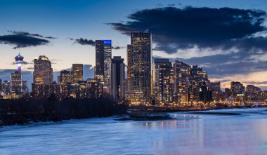 Alacakaranlıkta Calgary Alberta Kanada 'daki Bow Nehri' ne yansıyan ofis binaları ve apartmanlarıyla bir Kanada şehri..