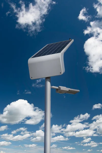 A solar powered street light on a lamp post recharging in the sun on a cloudy summer day.