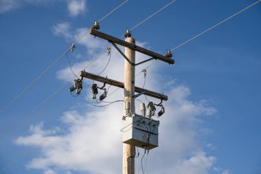 Mavi bir arka plan altında iletişim ve iletişim hatları olan tahta bir elektrik direği ve trafo..