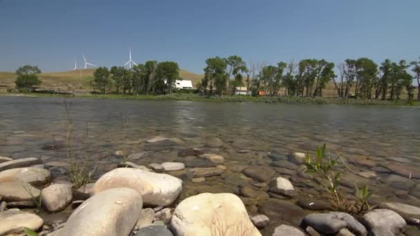 カナダの川の岩やバックグラウンド風車に沿ったパンニング運動 — ストック動画