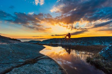 Şafak vakti kıyı koyundaki kayalıklarda duran sırt çantalı bir adamın görüntüsü.