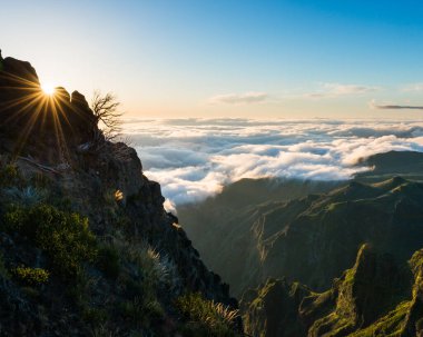 Güneş ışığı bir dağ uçurumundan ve bulutlarla dolu bir vadiden akıyor.