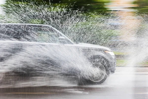 Hızlı bir arabanın su birikintisine girdiği ve kenarlara su sıçrattığı anın görüntüsü