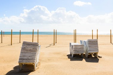 Arka planda şemsiyeleri ve katlanır güneşlikleri olan boş bir sahil..