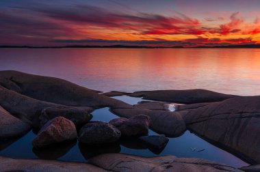 İsveç, Göteborg 'un kayalık kıyı şeridi boyunca güneş okyanusun üzerinde batar. Kayaların üzerindeki su gölleri alacakaranlıktaki renkli gökyüzünü yansıtır..