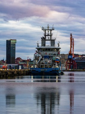 İsveç sahil güvenlik gemisi Gothenburg limanında demirlemiş durumda. Etrafı sakin sularla çevrili. Gece boyunca gökyüzü bulutlu ve modern binaları yansıtıyor..