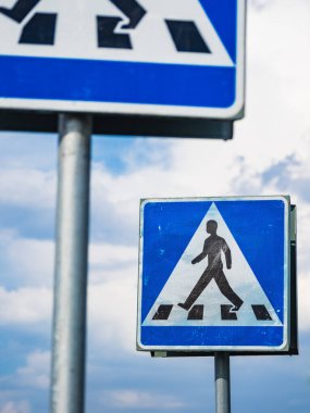 İsveç 'te açık mavi bir gökyüzünde yaya geçidi işareti belirgin bir şekilde görülüyor. Tabela, yayalar için güvenli bir geçiş bölgesini gösteren zebra haçı üzerinde yürüyen bir figür içeriyor..