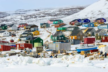 Renkli binalar kışın Qaanaaq köyünün manzarasını doldurur. Kar zemini kaplıyor. İnsanlar, doğa ve yapılar arasında günlük faaliyetlere katılıyor ve çalışıyorlar..