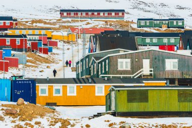 Grönland 'da bir köy olan Qaanaqq' ta insanlar yolda yürüyor. Caddelerde renkli binalar var. Kar, parlak güneş ışığı altında her yeri kaplar..