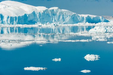 Buzdağları Grönland 'daki Ilulissat fiyortlarının sakin sularında sürükleniyor. Güneş buzun üzerinde parlıyor, suda yansımalar yaratıyor. Bu sahne Grönland 'ın doğasının özünü yansıtıyor..