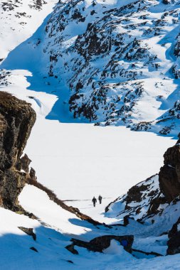 Grönland, Ilulissat yakınlarındaki dağlarda iki yürüyüşçü geniş bir kar ve buz sahasında yürür. Sahne karlı araziyi ve dik kayalıkları gösteriyor..