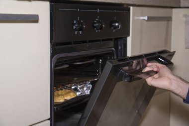 Adam fırındaki yiyecekleri kontrol ediyor.