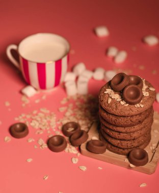 Pembe arka planda tahta tepside bir yığın yulaflı kurabiye. Yulaf ezmesi, çikolata şekeri. Ev yapımı kekler, tatlı kahvaltı, atıştırmalık. Şekerlerin parlak fotoğrafı.