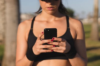 Şapkalı atlet kız akıllı telefona bakıyor.