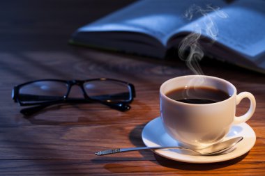 Fincan kahve, açık bir kitap ve bir masa üzerine gözlük.