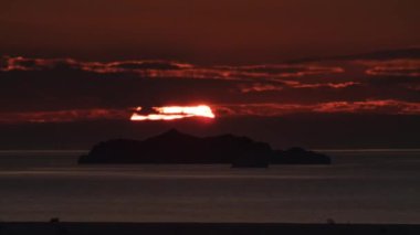 Deniz gölünde gün doğumu zaman aşımı. Okyanus suyu ve ada siluetinin üzerinde devasa bir güneş doğuyor.