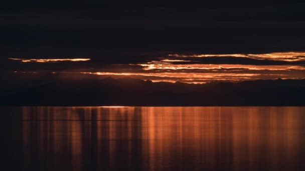 Lasso di tempo di raggi di luce del sole attraverso nuvole scure sul lago. Drammatico rosso arancio luminoso tramonto alba — Video Stock