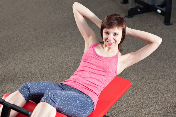 Leende kvinna träning med utbildning maskin i gymmet — Stockfoto