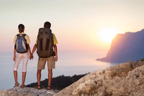 Paar op zoek bij zonsopgang uit hoge rots — Stockfoto