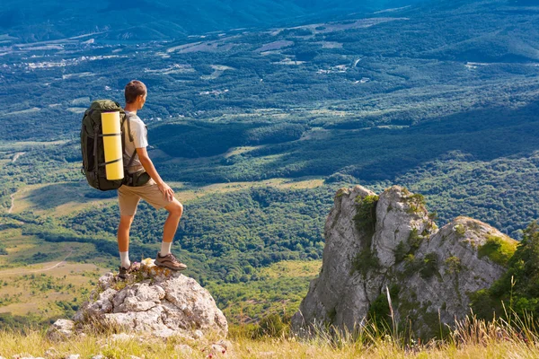 Backpacker na wysokiej skale i patrząc na duże zielone doliny — Zdjęcie stockowe