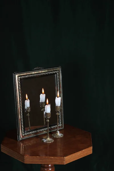 Mystic still life with mirror, reflection and two burning candles. Halloween concept, black magic ritual or spell with occult and esoteric symbols, divination rite. Vintage objects on witch table. reflection of a candle flame in a mirror in the dark.