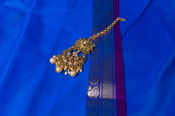 Indian traditional gold Indian wedding women\'s jewelry tika on blue saree background. Close-up. Still-life.