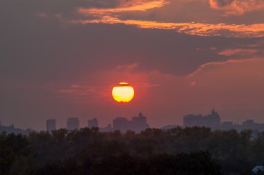 Şehrin üzerinde bulutlu gün batımında güneş 