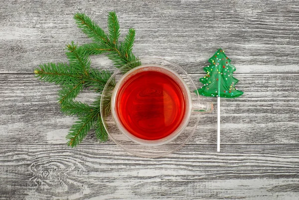 Tasse à thé en verre et bonbons de Noël sur fond en bois avec décor naturel de branches de pin, vue sur le dessus — Photo