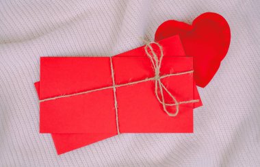 Beyaz örülmüş arka planda sevgililer günü için ipli kırmızı zarflar ve kırmızı kalp.