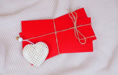 Beyaz örülmüş arka planda tatil için ipli kırmızı zarflar ve beyaz kalp, üst görünüm.