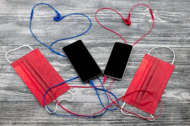 Tıbbi maskeler ve kalpli iki akıllı telefon ahşap arka planda kulaklık şeklinde. Üst görünüm, maket