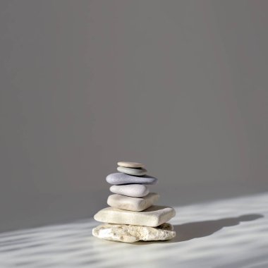 Gri zemin, güneş ışığı ve gölgelerde dengeli Zen taşları. Boşluğu kopyala, kare resim