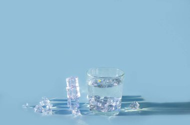 Mavi arkaplanda buz küpleri olan bir bardak su, boşluğu kopyala