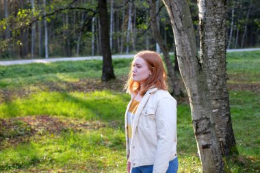 Girl with red hair in the park in autumn season, sunny day