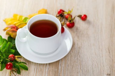 Tahta bir yüzey üzerinde taze gül üzümlü bir peçetede bir fincan çay.