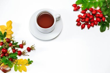 Beyaz bir yüzey üzerinde beyaz bir fincan gül çiçeği çayı, yanında taze gül üzümü, metin için bir yer.