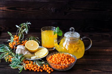 Koyu ahşap bir yüzeyde limonlu, zencefilli ve ballı deniz dikenli çay.