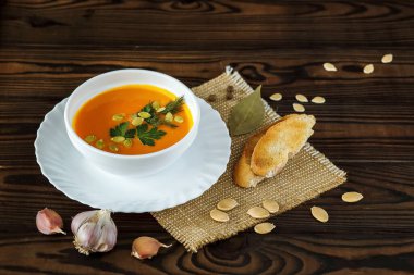 Hafif bir arka planda tohumlar ve otlarla süslenmiş beyaz bir kasede vejetaryen balkabağı kreması çorbası.